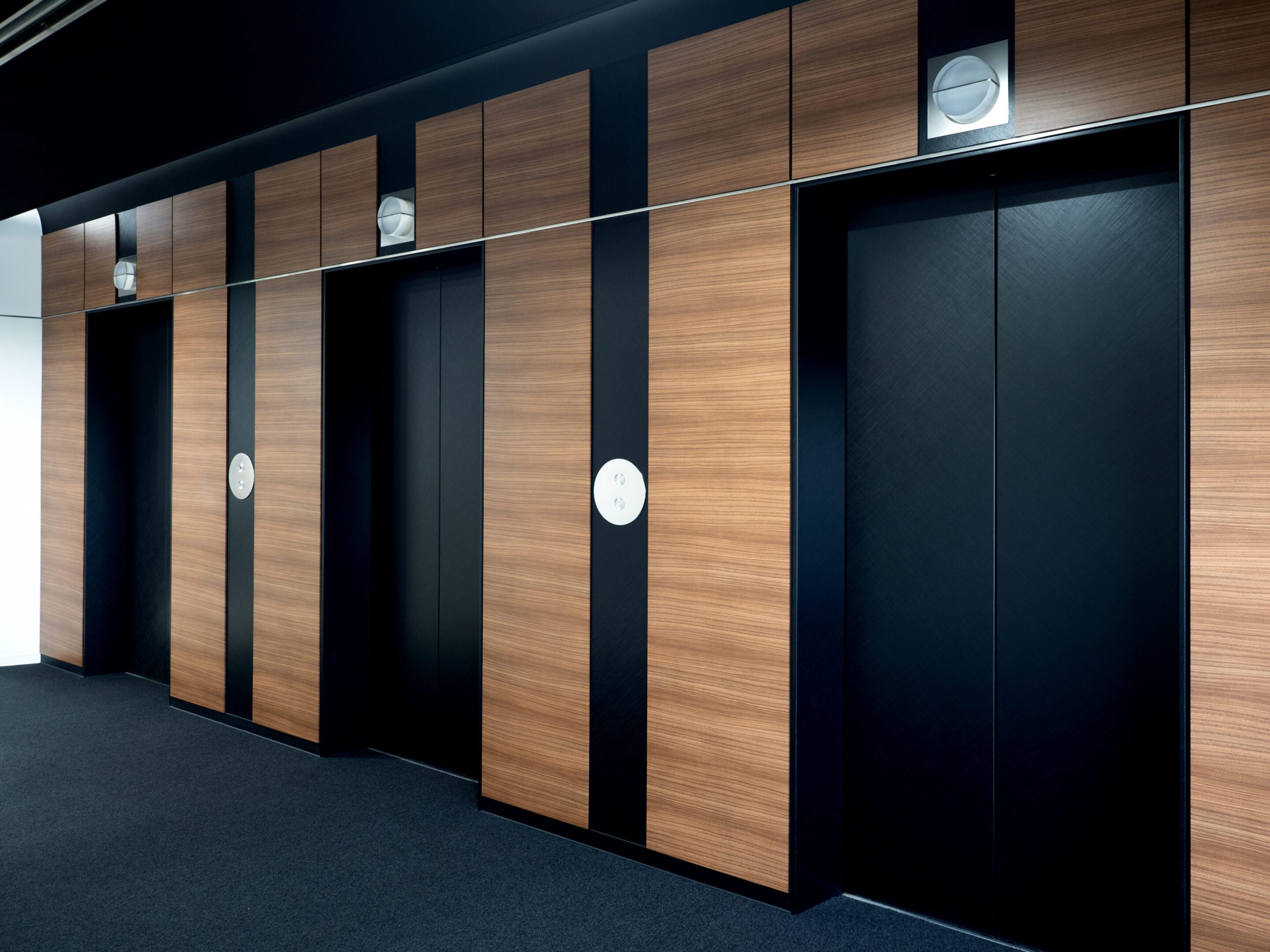 Wood-paneled elevator bank with dark metal entrances in a commercial building